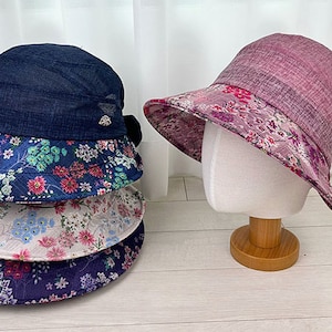 Peut inclure: Deux chapeaux bob réversibles avec des motifs floraux. Un chapeau est bleu marine avec un imprimé floral sur le dessous, et l'autre est rose avec un imprimé floral sur le dessous.