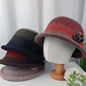 May include: Two felt hats with a striped pattern in shades of brown, red, and green. Each hat has a decorative flower accent.