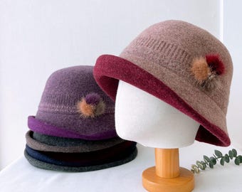 Puede incluir: Una pila de cuatro sombreros de fieltro con una banda de color contrastante alrededor de la parte inferior. El sombrero de arriba es de color marrón claro con una banda burdeos y un pequeño pompón marrón y negro. El segundo sombrero es morado con una banda morada y un pequeño pompón marrón y negro.
