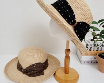 May include: Two straw hats with brown and black ribbon bows. The hats are on a wooden stand. The hats are a light brown color and have a wide brim.