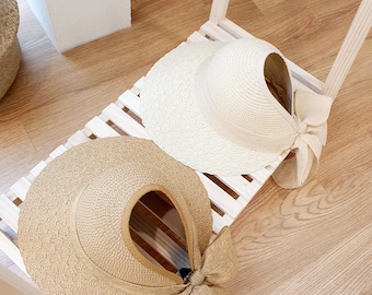 May include: Two straw sun hats with wide brims and bows. The hats are beige and brown and are displayed on a wooden shelf.
