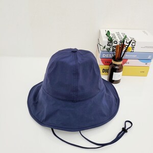 May include: A navy blue bucket hat with a wide brim and a black drawstring. The hat is made of a lightweight fabric and has a simple design.