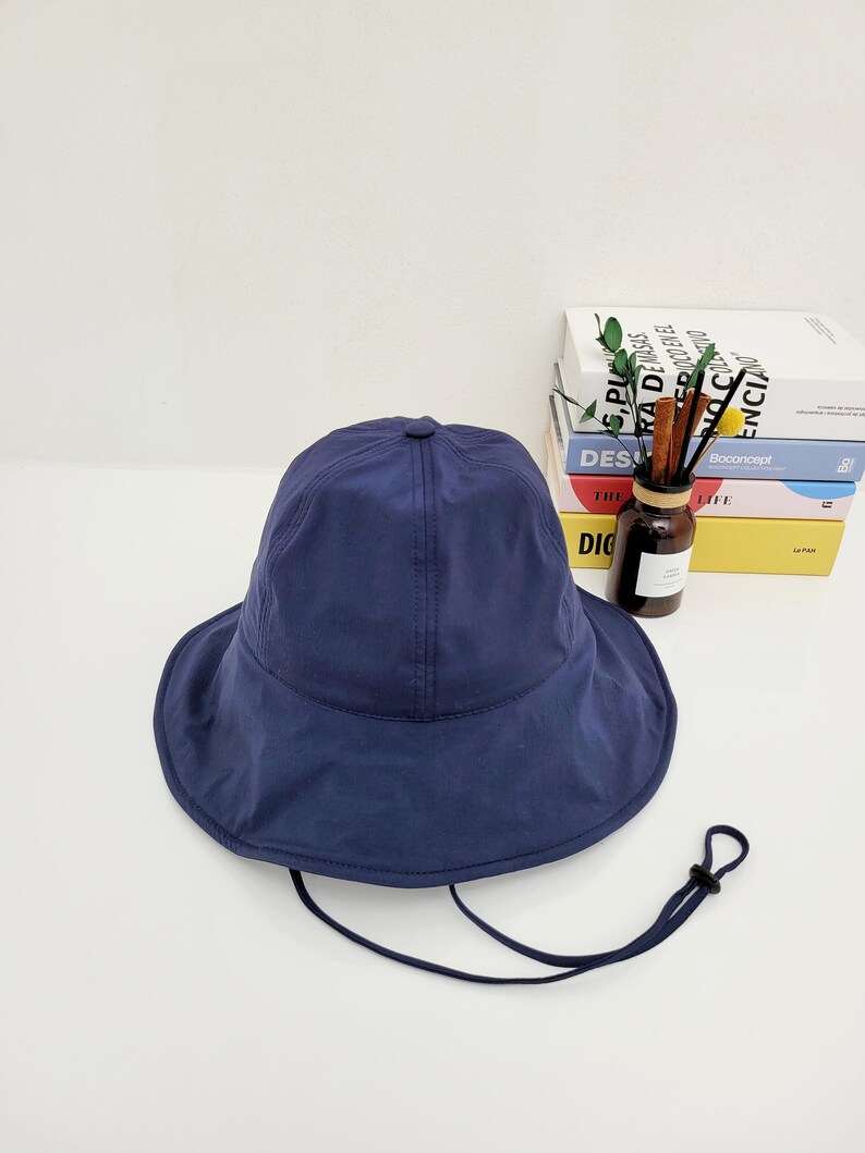 May include: A navy blue bucket hat with a wide brim and a black drawstring. The hat is made of a lightweight fabric and has a simple design.