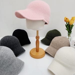 May include: A set of eight knitted baseball caps in various colors, including pink, gray, black, white, and brown. The caps have a curved brim and a soft, comfortable feel.