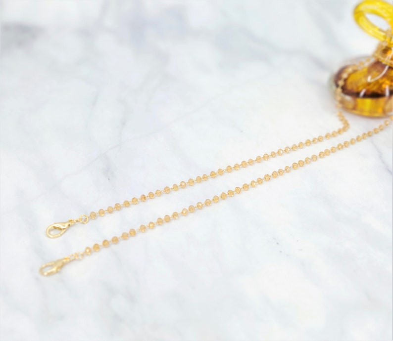 K&ouml;nnte beinhalten: Zwei goldene Ketten mit klaren Glasperlen. Die Ketten haben Karabinerverschl&uuml;sse.