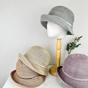 May include: Three straw hats in different colors and styles. The hats are all made of a woven material and have a wide brim. The hats are on a white surface.