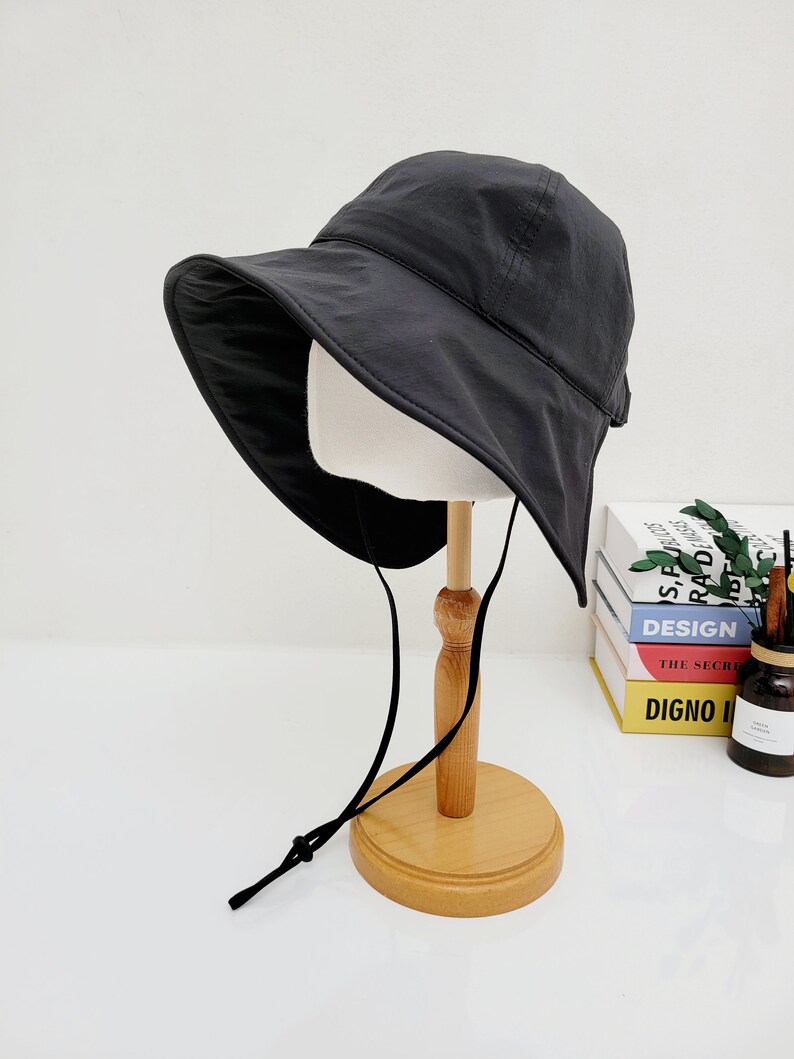 May include: A black leather bucket hat with a wide brim and a chin strap. The hat is on a wooden stand.