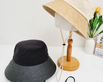 May include: Two bucket hats with a contrasting fabric and straw brim. The hat on the left is black with a black straw brim. The hat on the right is beige with a beige straw brim. Both hats have a black drawstring.