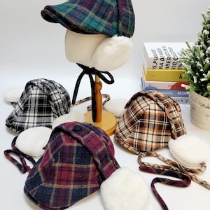 May include: A collection of plaid newsboy caps with faux fur ear flaps. The caps are in various colors, including green, black, brown, and burgundy, and are displayed on a white surface. Each cap has a matching tie.