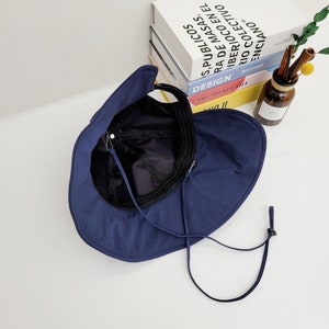 May include: A navy blue sun hat with a wide brim and a chin strap. The hat is folded in half and the inside of the hat is visible.