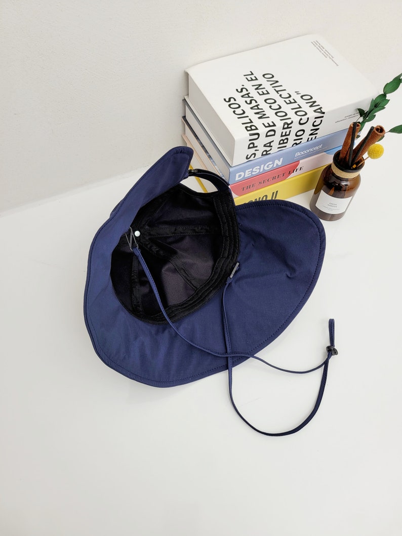 May include: A navy blue sun hat with a wide brim and a chin strap. The hat is folded in half and the inside of the hat is visible.