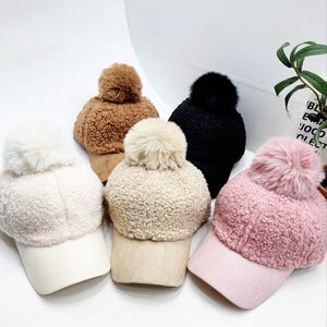May include: Four fuzzy pom-pom hats with suede brims in brown, cream, black, and pink.