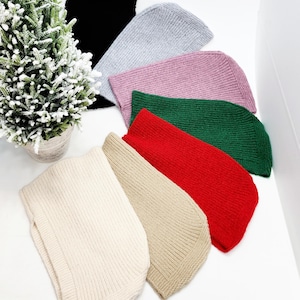 May include: Seven knitted beanies in various colors, including black, gray, pink, green, red, beige, and white. The beanies are arranged in a semi-circle on a white surface.