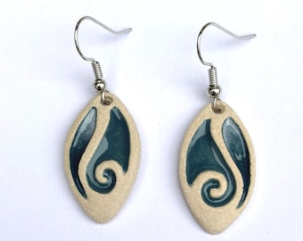 May include: A pair of ceramic earrings. Each earring has a cream-coloured, oval base with a teal swirl design. The earrings are suspended from silver-coloured, hypoallergenic ear wires.