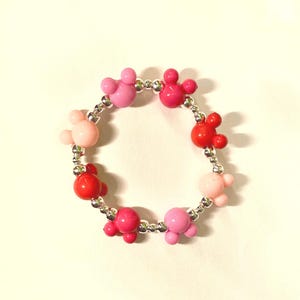 Pode incluir: Um bracelete de contas rosa e vermelho com contas em forma de Mickey Mouse.