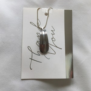 May include: A silver spoon pendant necklace with a silver chain. The pendant is shaped like a spoon with a rounded end. The necklace is displayed on a white card with the text "Thank You Mom" written in silver cursive.