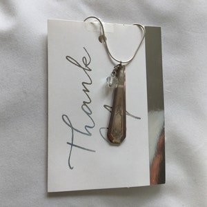 May include: A silver necklace with a charm made from a vintage spoon and a crystal bead. The necklace is hanging on a white card with the word "Thank" written in cursive.