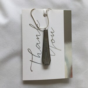 May include: A white card with silver lettering that says "Thank You". A silver spoon is attached to the card with a silver chain.