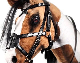 May include: A brown and white horse head with a black leather bridle and reins. The horse has a black mane and tail.
