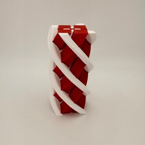 May include: A 3D-printed sculpture featuring a woven design of red and white elements. The sculpture has a cylindrical shape with a spiraling pattern. The red sections are rectangular, and the white sections are curved.