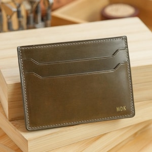 May include: A dark green leather card holder with two card slots and the initials "MDK" embossed in gold on the front.
