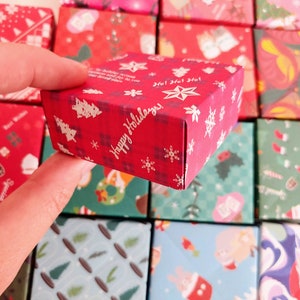 May include: A collection of small red and green gift boxes with various Christmas patterns. The boxes are decorated with snowflakes, trees, and the words "Happy Holidays!" and "Ho! Ho! Ho!"