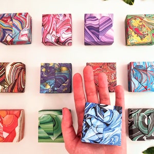 May include: Ten small, square boxes with a heart-shaped design on each side. The boxes are made of paper and have a marbled pattern in various colors, including red, blue, green, purple, and yellow.