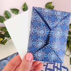May include: A white envelope with a blue and white patterned envelope inside. The pattern features a repeating design of white circles with blue lines radiating outward.