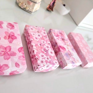 May include: Four pink boxes with a floral pattern of cherry blossoms. The boxes are lined up in a row from left to right.