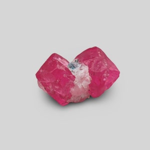 May include: A cluster of pink, red, and white crystals. The crystals are translucent and have a glassy luster. The crystals are arranged in a cluster, with some of the crystals overlapping each other.