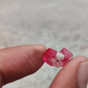May include: A small, pink, crystalline mineral with a white, cloudy center. The mineral is being held in a hand.