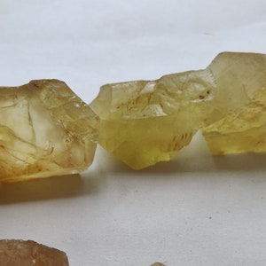 Puede incluir: Cuatro cristales facetados transl&uacute;cidos de color amarillo con una textura natural rugosa. Los cristales est&aacute;n dispuestos en fila, con el cristal m&aacute;s grande a la derecha y el m&aacute;s peque&ntilde;o a la izquierda.
