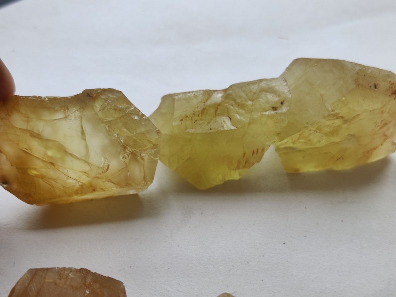 Puede incluir: Cuatro cristales facetados transl&uacute;cidos de color amarillo con una textura natural rugosa. Los cristales est&aacute;n dispuestos en fila, con el cristal m&aacute;s grande a la derecha y el m&aacute;s peque&ntilde;o a la izquierda.