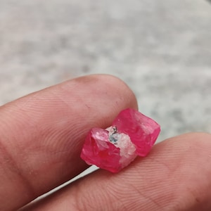 May include: A close-up of a pink crystal with a white center. The crystal is being held by a hand.
