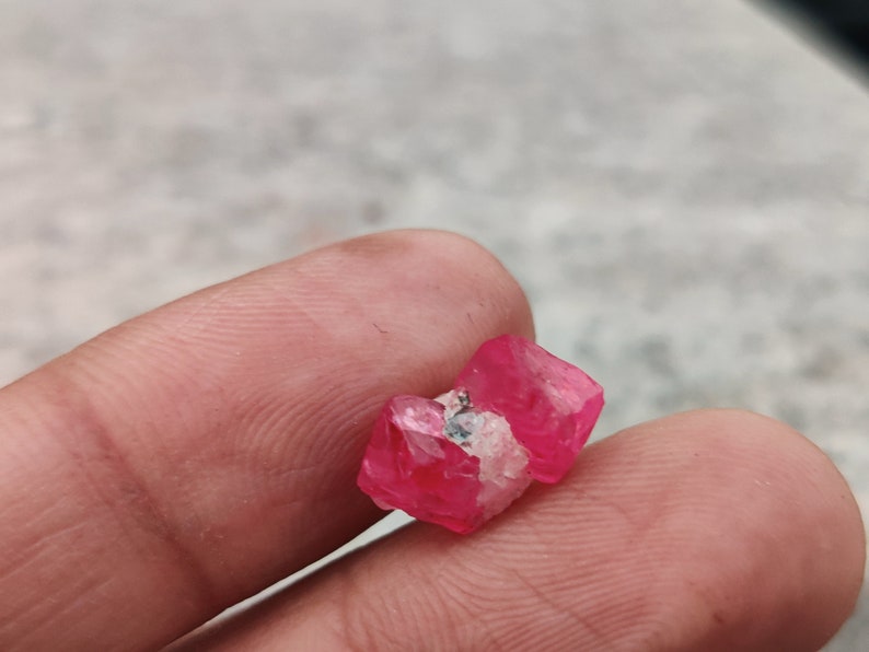May include: A close-up of a pink crystal with a white center. The crystal is being held by a hand.