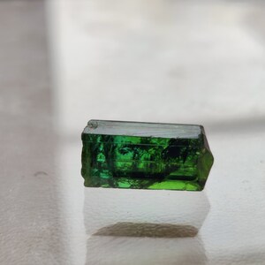 May include: A dark green, faceted, rectangular gemstone with a slight curve on one side.