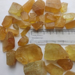 Puede incluir: Una colecci&oacute;n de cristales naturales en bruto, facetados, de color amarillo verdoso. Los cristales son de varios tama&ntilde;os y formas. Se incluye una regla para la escala, que muestra que los cristales miden aproximadamente de 2,5 a 7,5 cm de largo.
