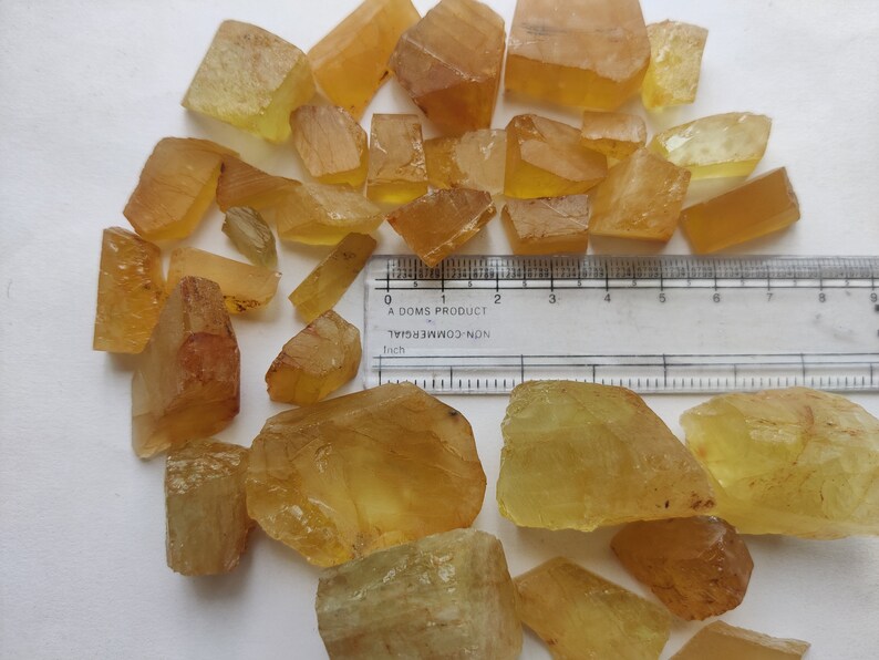 Puede incluir: Una colecci&oacute;n de cristales naturales en bruto, facetados, de color amarillo verdoso. Los cristales son de varios tama&ntilde;os y formas. Se incluye una regla para la escala, que muestra que los cristales miden aproximadamente de 2,5 a 7,5 cm de largo.