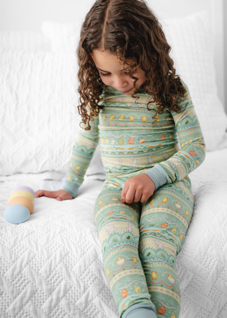Puede incluir: Conjunto de pijama de dos piezas para ni&ntilde;os, de color verde claro, con un estampado de tem&aacute;tica de Pascua. El pijama presenta una parte superior de manga larga y pantalones a juego con un dise&ntilde;o repetido de huevos, pollitos y conejitos. Los pu&ntilde;os son de color azul claro.