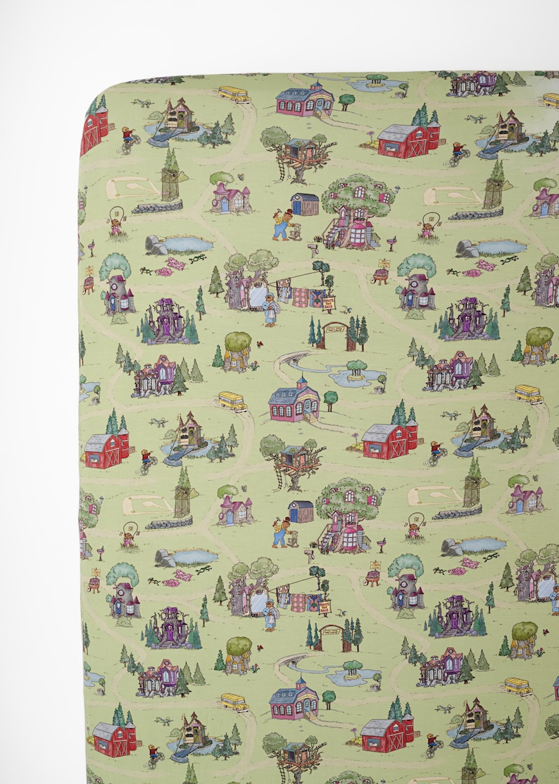 May include: A light green fitted cot sheet with a whimsical map design. The map features houses, trees, roads, and people. The houses are red, purple, and pink. The roads are tan, and the trees are green.
