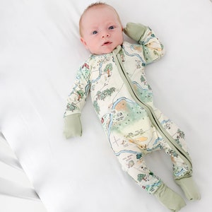 May include: A baby wearing a green and white map-print footed pajamas with a zipper closure. The pajamas have green cuffs on the sleeves and legs.