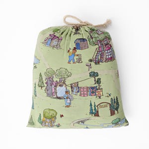 May include: A drawstring bag featuring a light green illustrated pattern of a village scene with houses, trees, and figures. The bag is tied with a natural rope. The design has a whimsical, storybook aesthetic, with a charming, playful feel.
