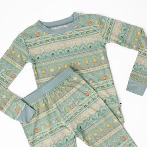 Puede incluir: Un conjunto de pijama de dos piezas en color verde azulado claro con un estampado tem&aacute;tico de Pascua. El estampado incluye conejitos, pollitos y huevos de Pascua. La parte superior de manga larga y los pantalones tienen un dise&ntilde;o a juego.