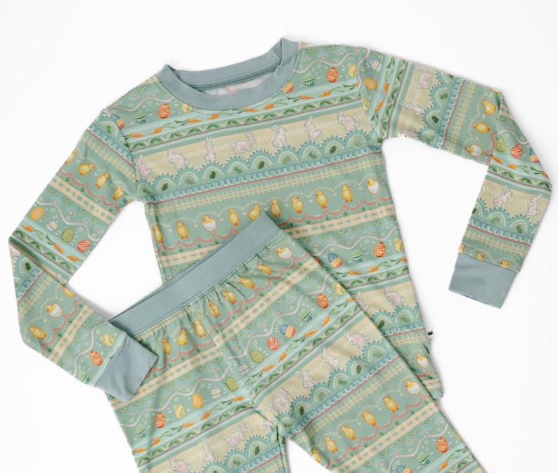 Puede incluir: Un conjunto de pijama de dos piezas en color verde azulado claro con un estampado tem&aacute;tico de Pascua. El estampado incluye conejitos, pollitos y huevos de Pascua. La parte superior de manga larga y los pantalones tienen un dise&ntilde;o a juego.