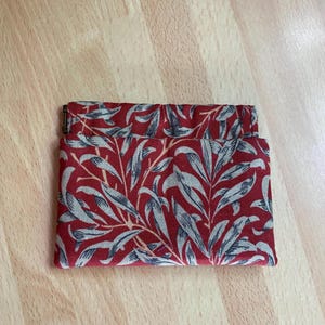 May include: A rectangular fabric pouch featuring a deep red background with a repeating pattern of light gray willow leaves and branches. The pouch has a folded top edge and a small metallic hinge visible on the left side of the opening.