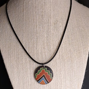 May include: A black cord necklace with a round pendant featuring a geometric design in shades of red, green, blue, and black.