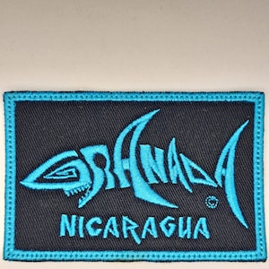 Könnte beinhalten: Ein blauer und schwarzer gestickter Aufnäher mit einer stilisierten Hai-Silhouette und dem Text "Sharks" und "Nicaragua".