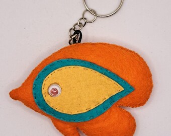 May include: Orange felt fish keychain with a yellow felt fin and a blue felt outline. The fish has a red button eye.