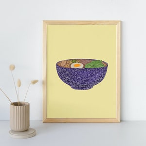 May include: A framed print of a yellow background with a purple bowl of ramen noodles. The bowl has a white floral pattern. The ramen has a soft boiled egg, green onions, and other ingredients.