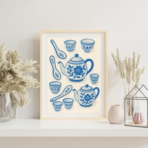 May include: A framed illustration of a blue and white teapot and teacups with floral designs. The illustration is surrounded by a white background.